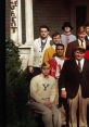 Cast of "Animal House" in iconic poses outside the fraternity house, showcasing classic collegiate styles and humor.