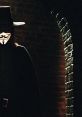 V from V for Vendetta, cloaked figure with iconic Guy Fawkes mask and hat, standing in shadowy corridor.