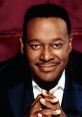 Luther Vandross smiling warmly with hands clasped, showcasing his iconic style and soulful presence in music.