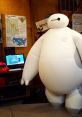 Baymax stands in a cozy room, surrounded by educational posters and a computer, showcasing a friendly, inflatable design.