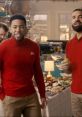 Two men in red sweaters enjoy a playful moment in a State Farm commercial setting with a festive table backdrop.