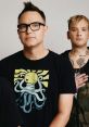 Mark Hoppus and Matt Skiba of blink-182 pose together, showcasing their unique style and band merchandise in a studio setting.