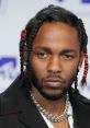 Kendrick Lamar with intricate braids and a statement necklace, showcasing his distinct style at a public event.