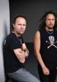 Lars Ulrich and Kirk Hammett of Metallica pose coolly, showcasing their iconic style and rock spirit in a dramatic setting.