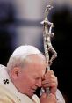 Pope John Paul II praying with his unique crucifix, symbolizing faith and devotion during a solemn moment.