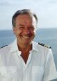 Smiling captain in a white uniform near the ocean, representing the spirit of "Traumschiff" voyages and adventures.