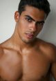 Attractive young Mexican man with chiseled features, showcasing a confident gaze and a toned physique against a neutral background.