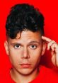 Rudy Mancuso with a thoughtful expression against a bright red background, showcasing his distinctive hairstyle and style.