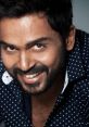 Karthi Vijay flashes a charming smile, showcasing his stylish look in a polka-dot shirt against a clean backdrop.