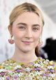 Saoirse Ronan appears elegantly styled with vibrant earrings and a colorful embellished dress, showcasing her unique fashion sense.