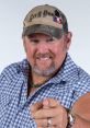 Larry the Cable Guy smiles and points energetically, wearing a plaid shirt and camo cap, embodying his comedic persona.