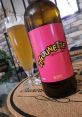 Zigounette au vent bottle with pink label beside a glass of blonde beer on a rustic table. Enjoy this refreshing brew!