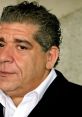 Close-up of Joey Diaz with curly hair, wearing a black suit and white shirt, showcasing his expressive features.