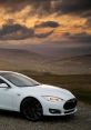 White Tesla Model S parked on a scenic hilltop with a dramatic sunset backdrop, showcasing electric vehicle innovation.