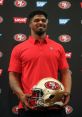 Dee Ford in a red San Francisco 49ers polo shirt holding a 49ers helmet at a press event, showcasing his team pride.