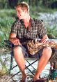 Young man sits on a camp chair by the beach, smiling and wrapped in a blanket, embodying summer vibes from "The Last Song.