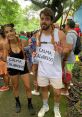 Two friends celebrate with "Calma, Calabreso" signs, playful costumes, and a lively crowd in a festive outdoor setting.