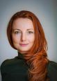 Portrait of a woman with long red hair and green eyes, wearing a dark green top, embodying elegance and confidence.