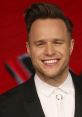 Olly Murs smiles broadly in a stylish suit, showcasing his charm and personality at a media event.