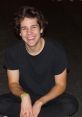 David Dobrik smiling while sitting casually in a black outfit, capturing the fun vibe of his popular vlogs.