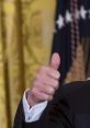 Donald Trump gives a thumbs-up gesture in a formal setting, symbolizing confidence and positivity.