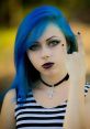 Young woman with blue hair and dark lipstick making a rock sign, embodying a bold metal aesthetic with stylish accessories.