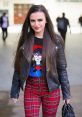 Cher Lloyd showcases a stylish look with a graphic tee, leather jacket, and red plaid pants, exuding confidence and charisma.