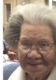 Smiling elderly woman with gray hair and glasses, showcasing warmth and wisdom in a cozy setting.