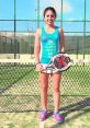 Nuria from Spain, dressed in sporty attire, poses with her paddle and smiles on a tennis court, showcasing her athleticism.