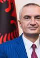 Ilir Meta, Albanian politician, poses confidently against a backdrop of the Albanian flag, showcasing national pride and leadership.